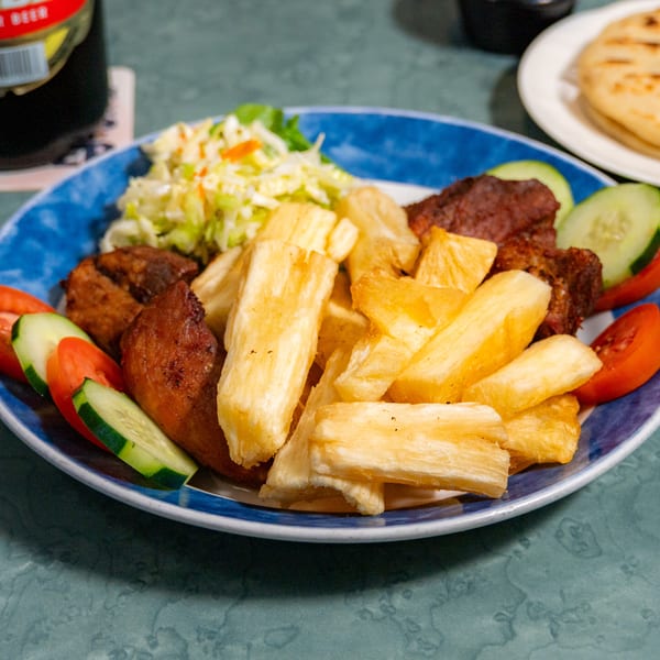 Plate of fried yuca, meat, coleslaw, and vegetables with a beer and flatbread in the background.