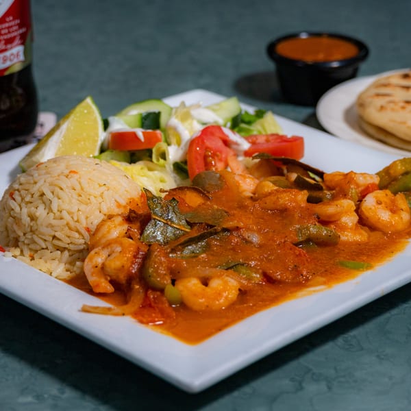 Shrimp in red sauce with rice, salad, and lime, alongside a Pilsener beer and flatbread.