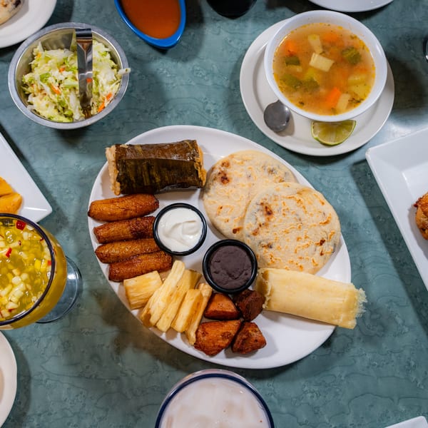 Restaurant table with a spread of Latin American food: pupusas, chicken, plantains, soup, and tamales.