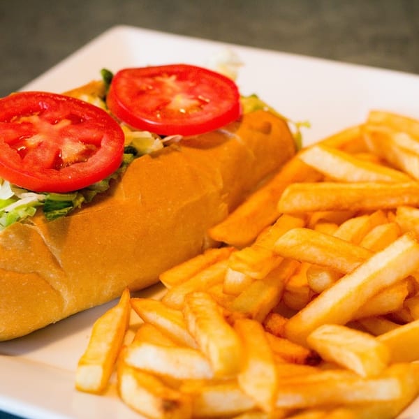 A sub sandwich with lettuce and tomato slices, served with golden french fries.